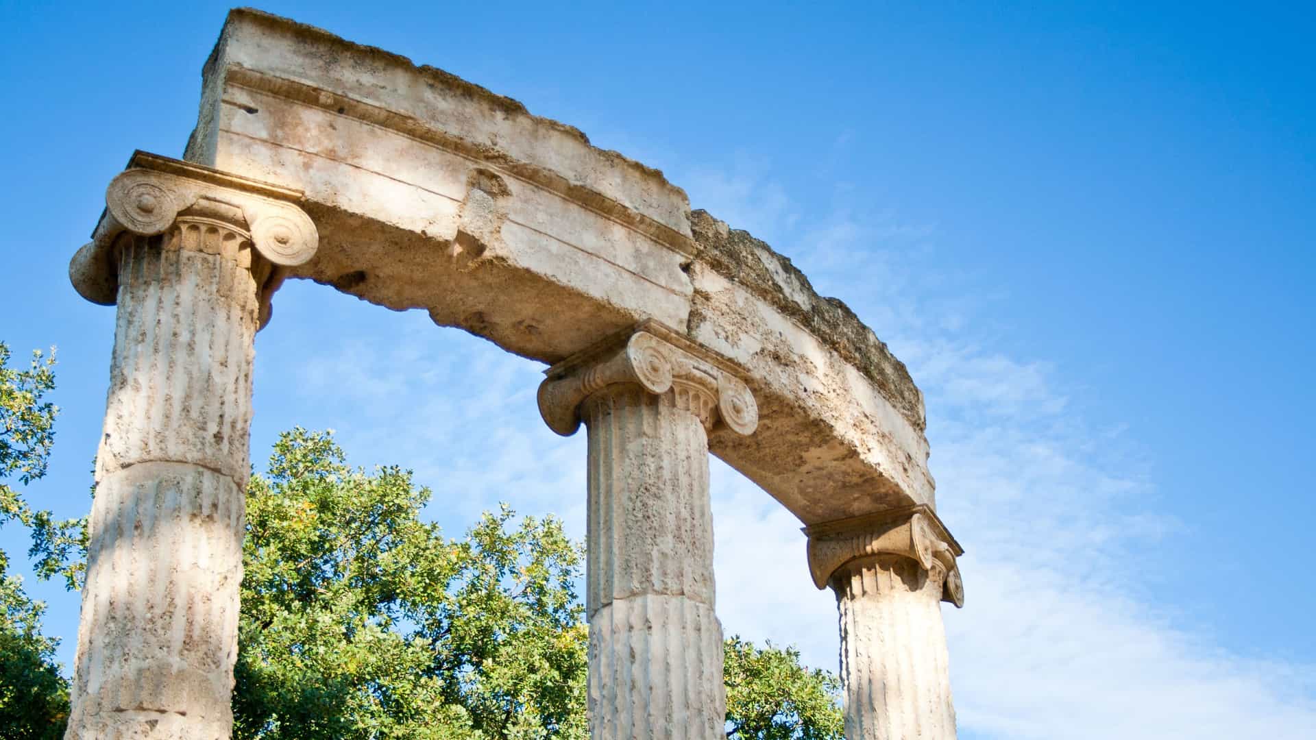 Looking up at the ancient stone columns of the Philippeion, with their distinctive scroll-like Ionic capitals, in the ruins of Olympia, near Katakolon, Greece.