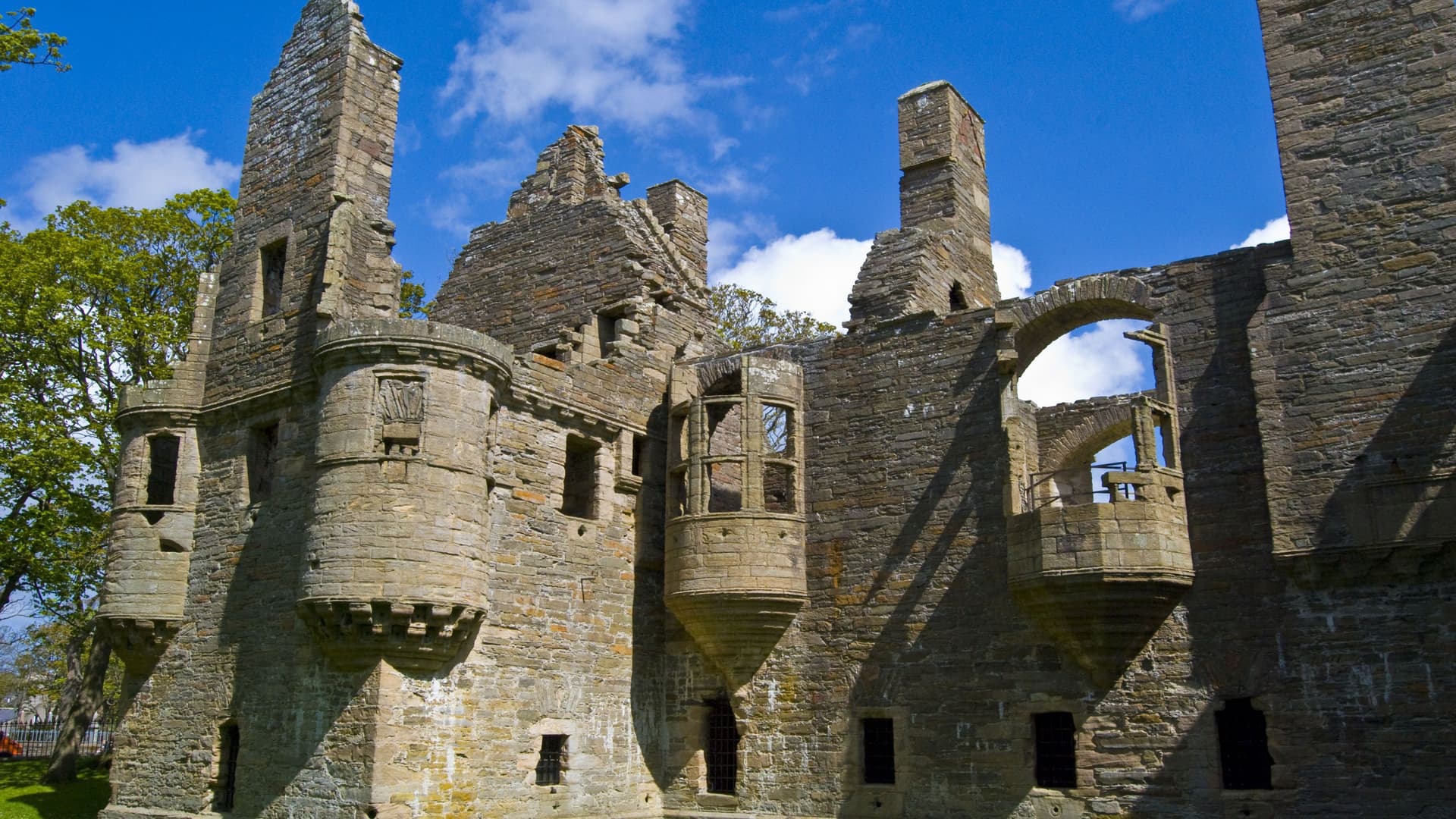 The impressive stone ruins of the Earl's Palace, a historic landmark in Kirkwall on the Orkney Islands, with detailed stonework and arches under a bright blue sky.