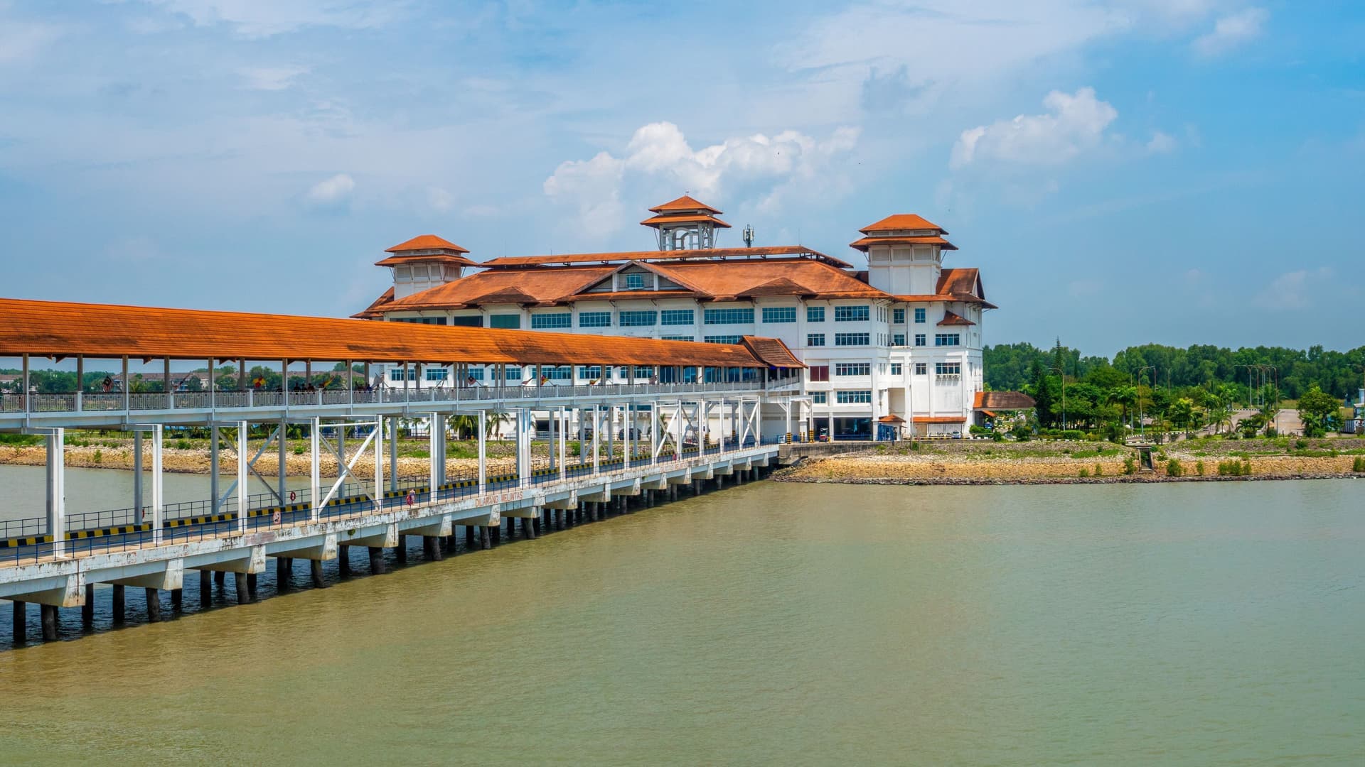 A view of the main cruise terminal building at Port Klang in Kuala Lumpur, Malaysia, with its unique architectural style, a long covered walkway, and the sea in front.