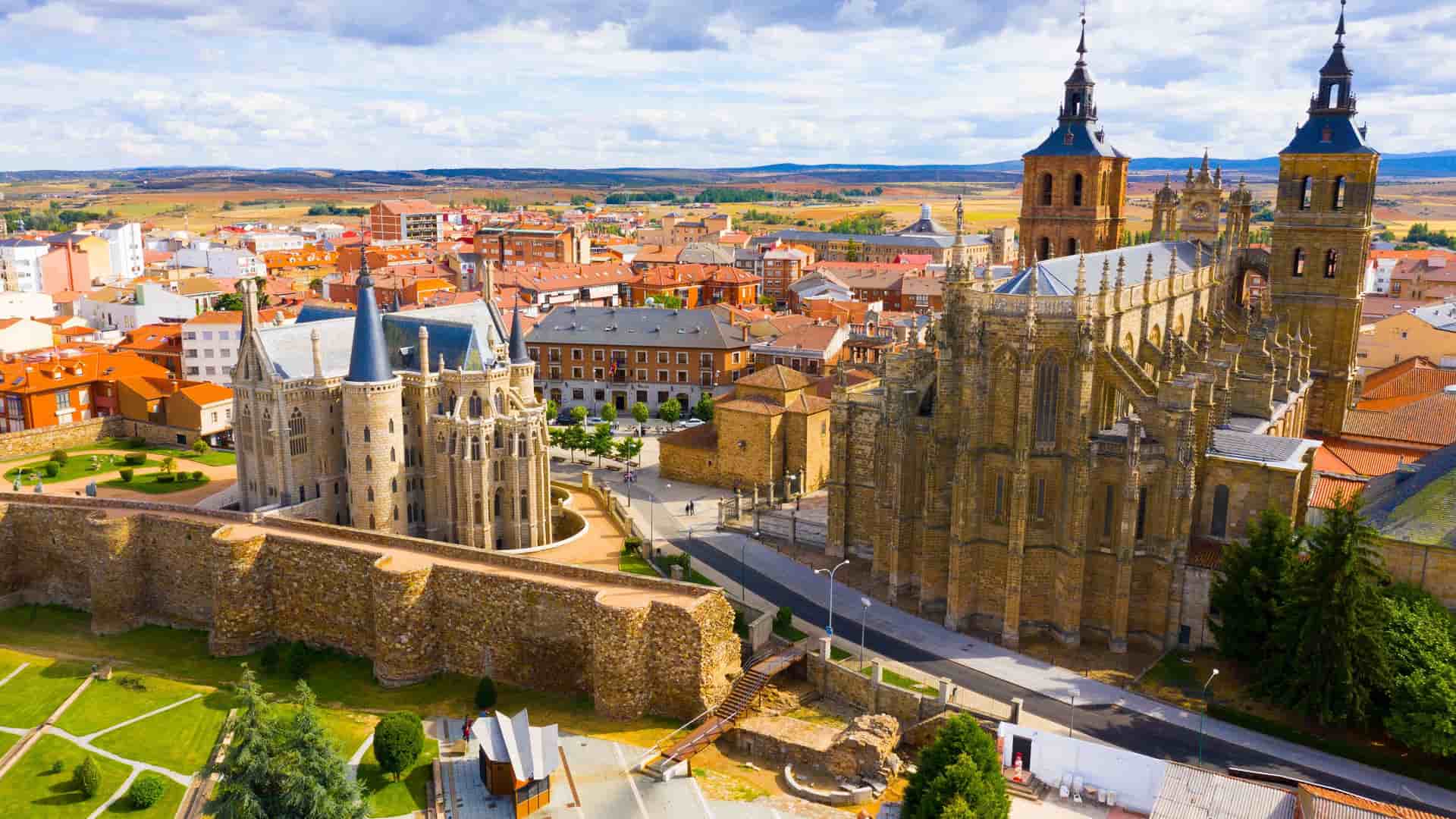 "An aerial view of Astorga's historic city center in León, Spain, featuring the Gaudi-designed Episcopal Palace and the imposing Astorga Cathedral with its twin bell towers. "