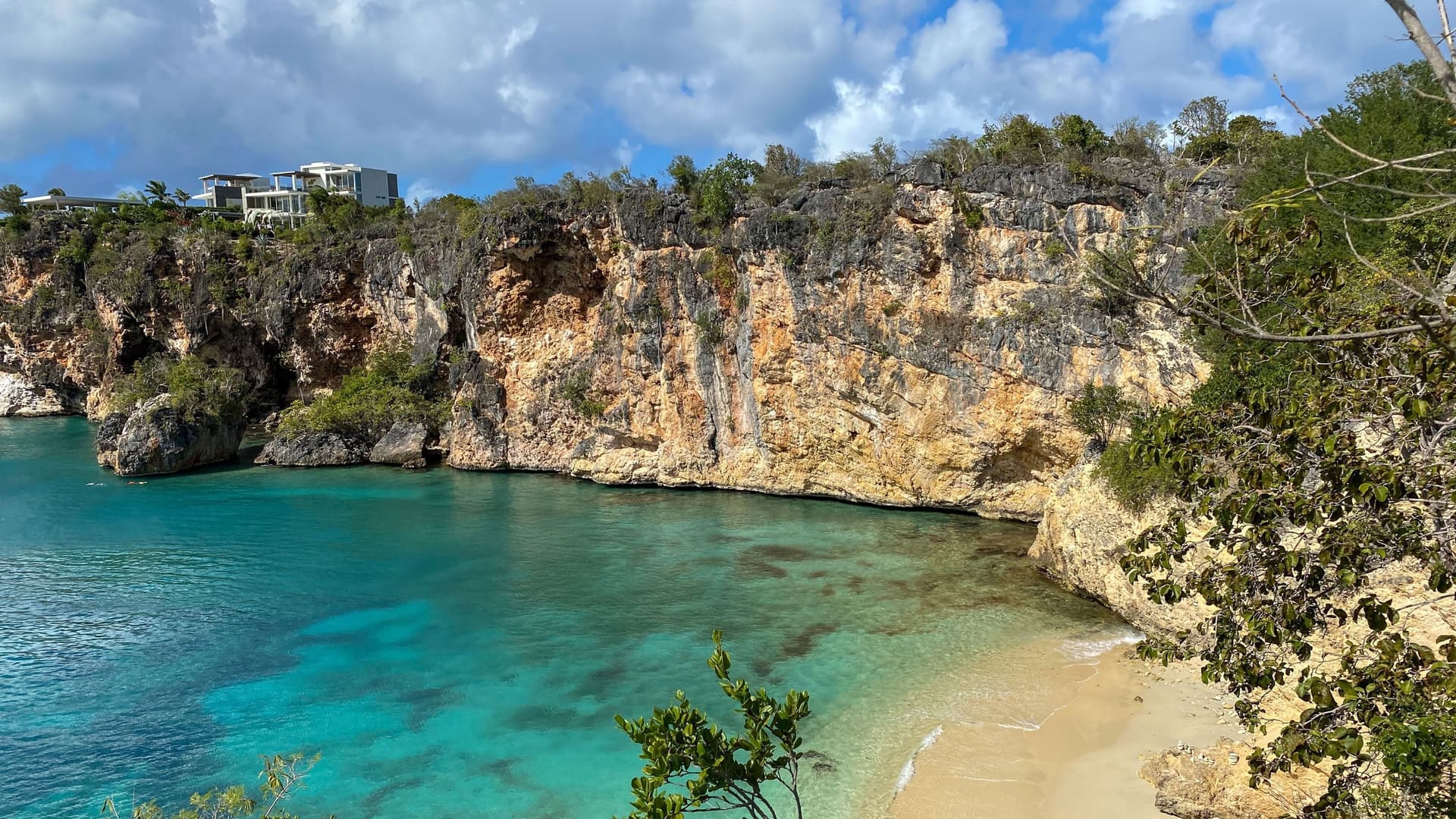 A stunning image of Little Bay in Anguilla, a secluded, beautiful beach with turquoise water surrounded by towering rocky cliffs and lush green vegetation.