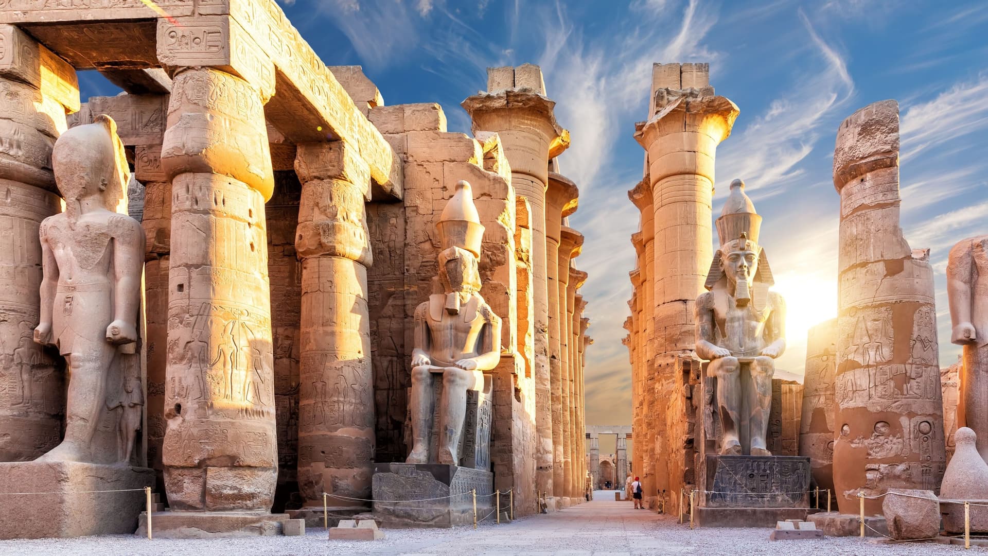A breathtaking sunset view of the ancient Luxor Temple in Egypt, showcasing towering statues of pharaohs, massive columns, and hieroglyphics bathed in golden light.