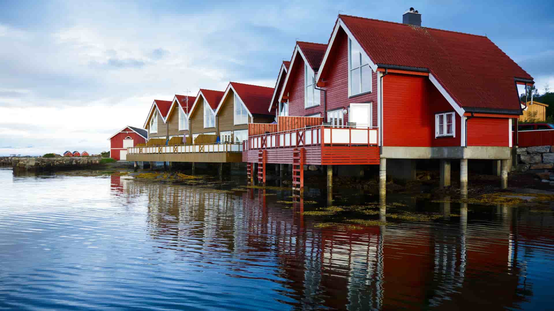 A picturesque row of traditional red wooden boathouses, known as "rorbuer," built on stilts over the tranquil waters of a fjord near Molde, Norway.
