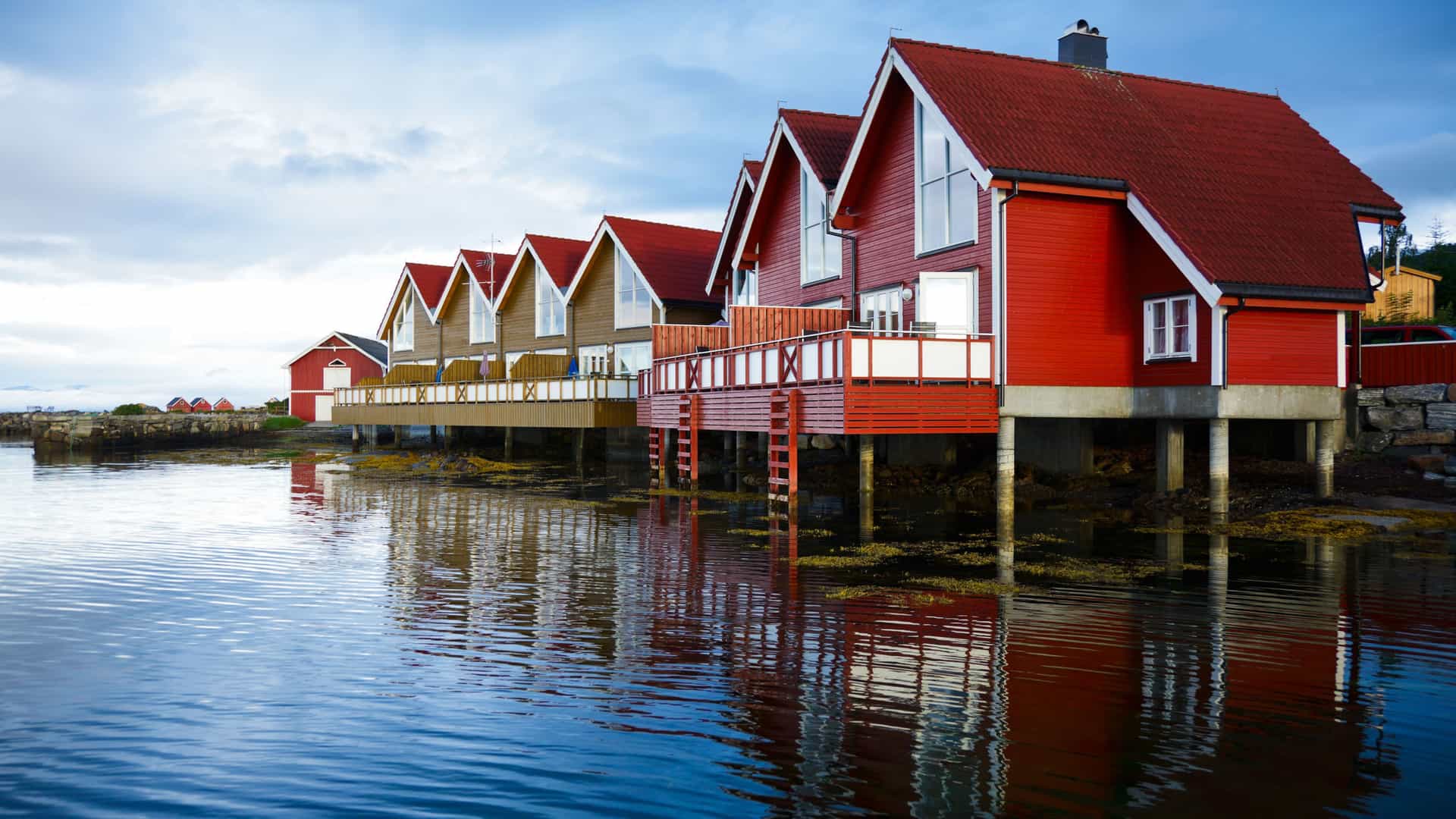 A picturesque row of traditional red wooden boathouses, known as "rorbuer," built on stilts over the tranquil waters of a fjord near Molde, Norway.