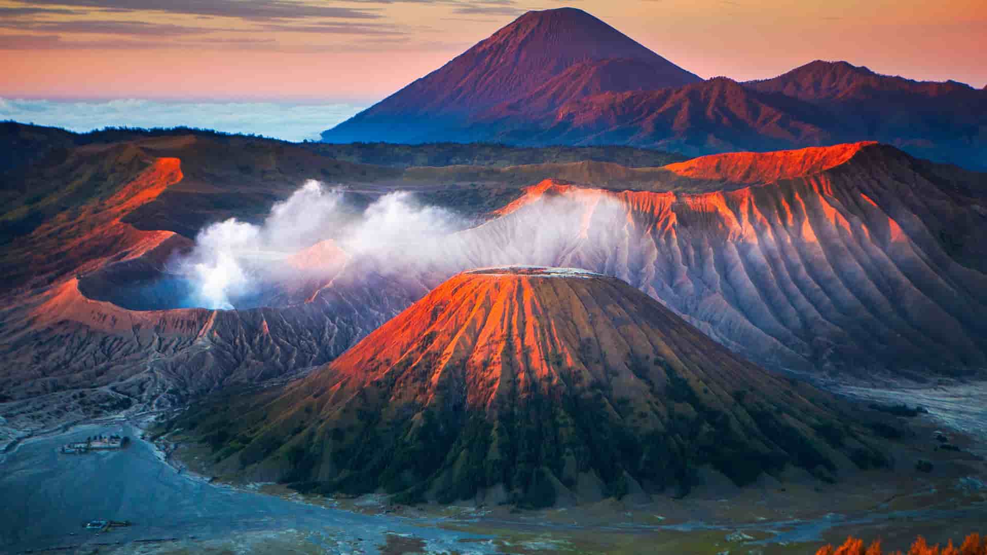 "An aerial panoramic sunrise view of the volcanic landscape in East Java, Indonesia, showcasing the smoking Mount Bromo crater and the surrounding Tengger caldera. "