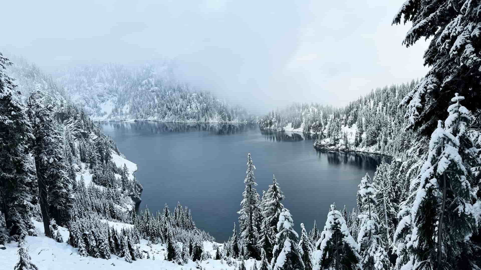 "A stunning panoramic shot of a serene winter landscape at Snow Lake, a popular hiking trail near North Bend, Washington, covered in fresh snow. "