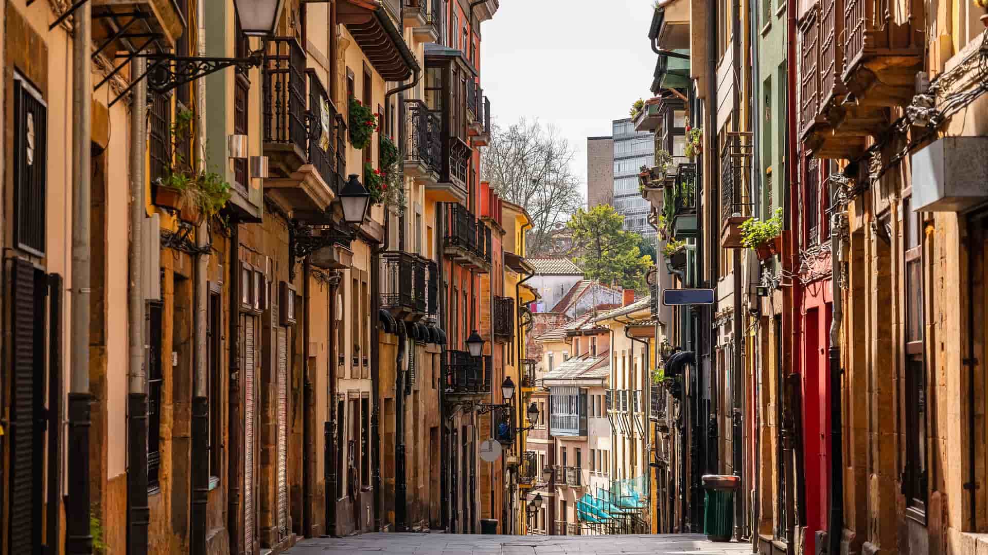 "A beautiful shot of a narrow cobblestone street in Oviedo, Spain, with historic buildings featuring colorful facades, balconies, and traditional lampposts. "