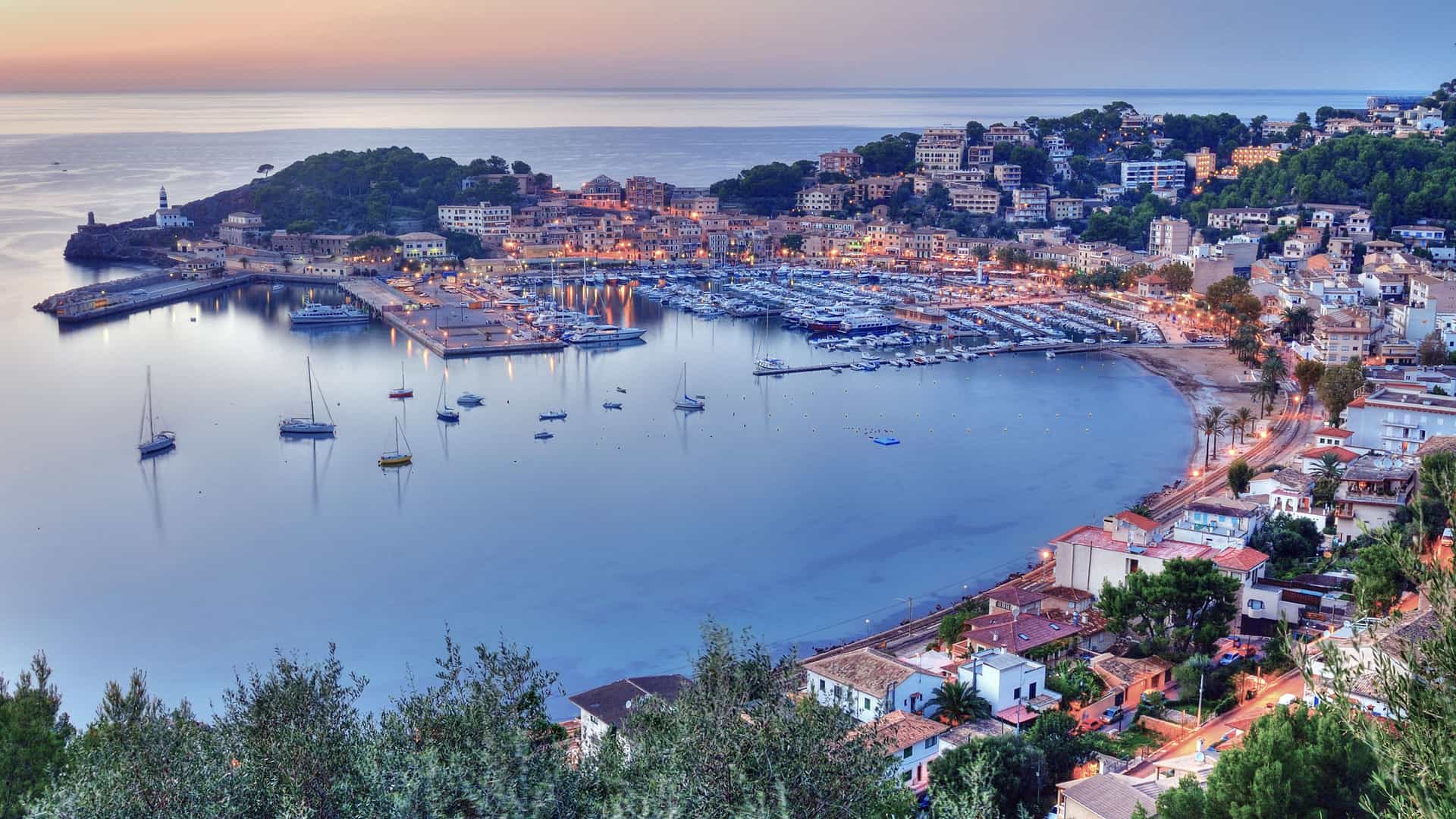 A panoramic sunset shot of the beautiful harbor in Palma de Mallorca, Spain, with a marina full of boats and buildings on the surrounding hills.