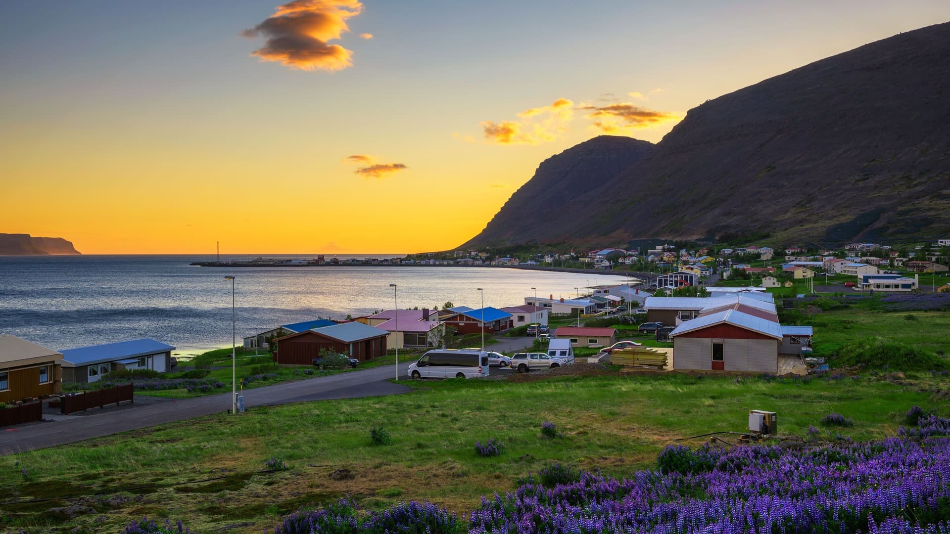 A view of the small fishing village of Patreksfjörður, Iceland, with colorful houses along the shore and a huge mountain in the background at sunset.