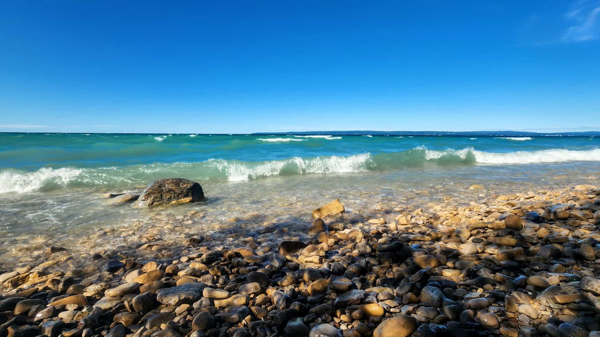 "A stunning low-angle shot of the clear blue waters of Little Traverse Bay, with small waves hitting the rocky shoreline near Petoskey, Michigan. "