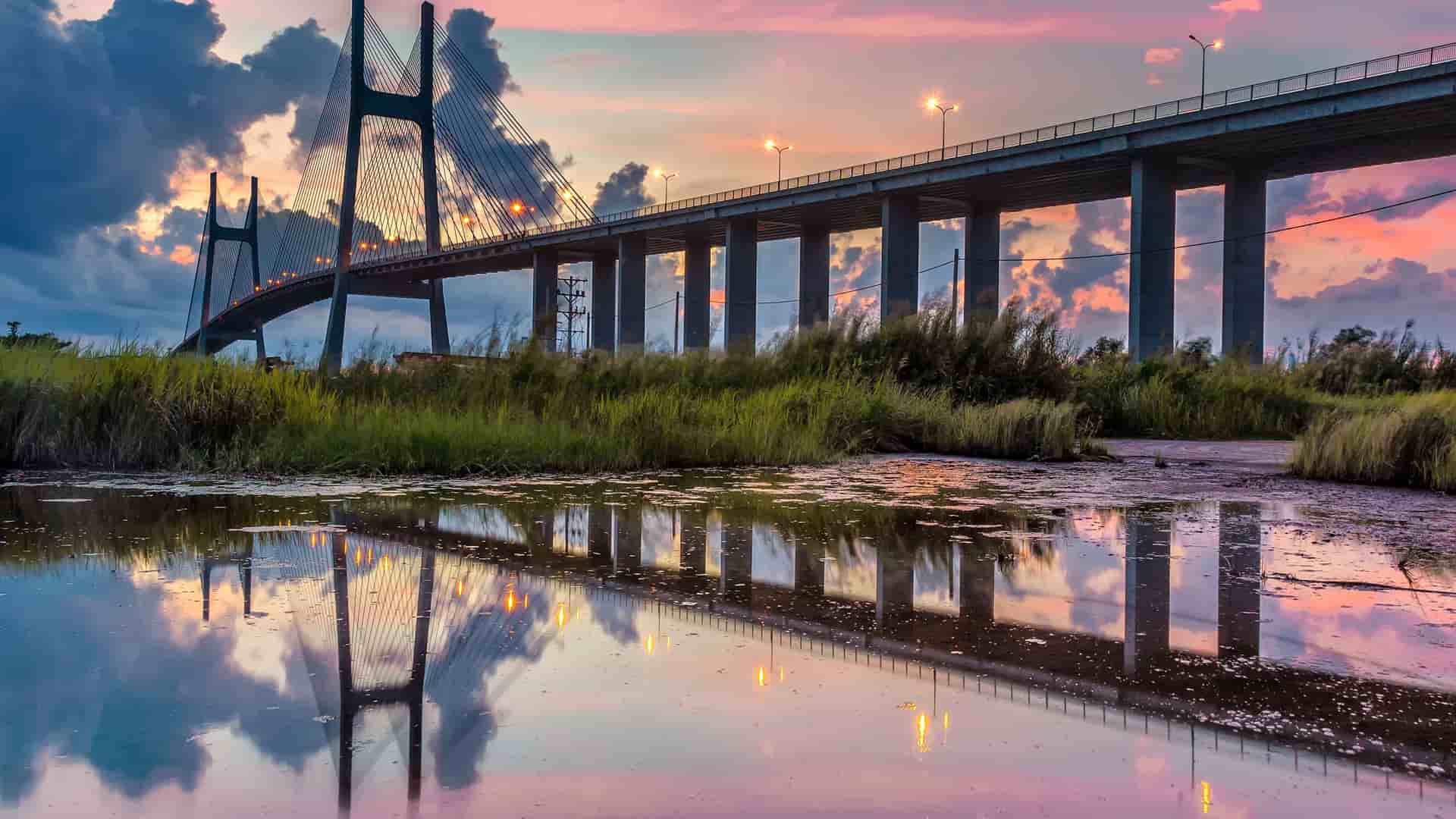 A view of a large, cable-stayed bridge and its reflection in the water at sunset, a landmark near the port of Phu My, Vietnam.