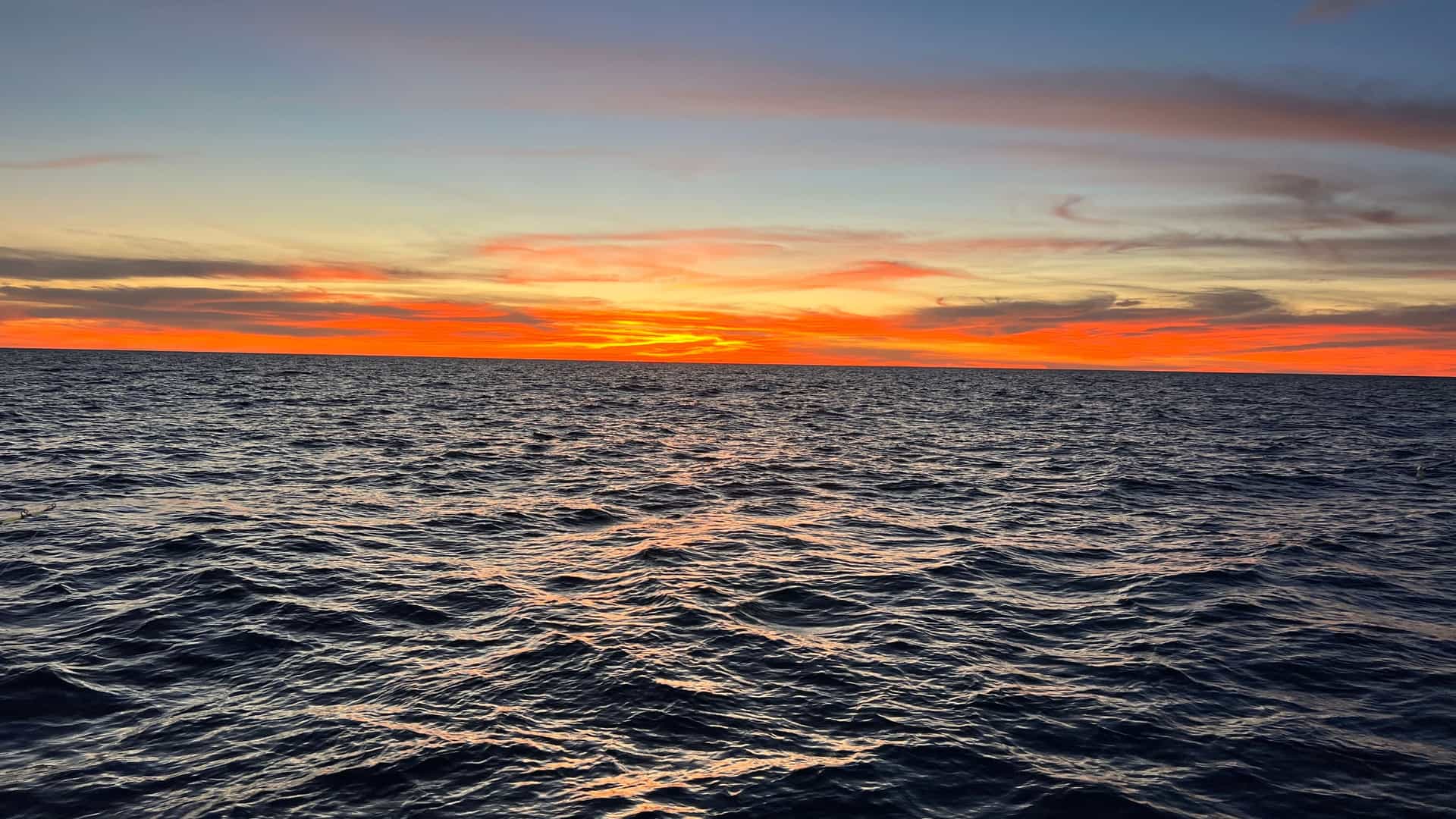 A wide-angle view of a fiery orange and red sunset over the deep blue, rippling waters of the South China Sea, with a straight horizon.