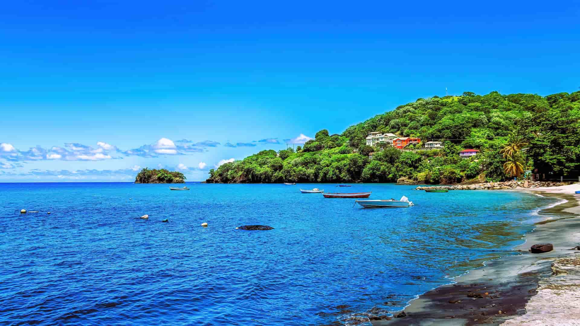 A scenic Caribbean bay near Kingstown, Saint Vincent and the Grenadines, with small boats anchored in the turquoise water and lush green hillsides with colorful houses.