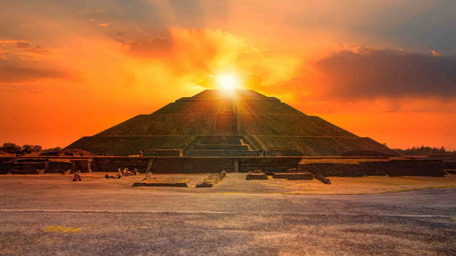 The large, stepped Pyramid of the Sun is silhouetted against a brilliant orange sunset in the ancient city of Teotihuacan.