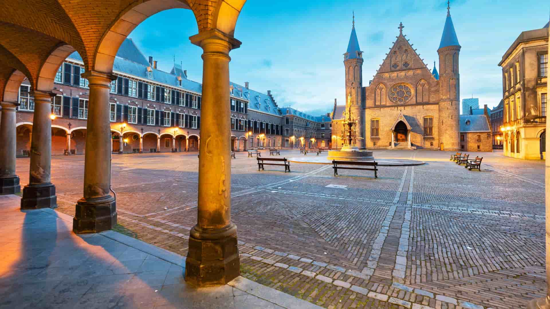 The Binnenhof courtyard features a gothic structure and archways, illuminated at dusk with benches across the cobblestone square.