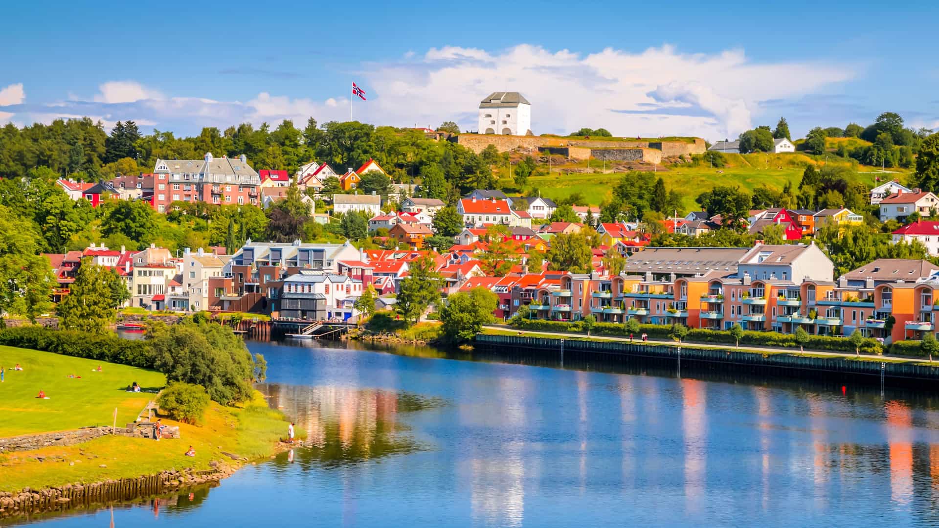 A panoramic view of Trondheim, Norway, with its colorful waterfront houses and charming historic buildings lining the Nidelva River, with the Kristiansten Fortress on the hill.