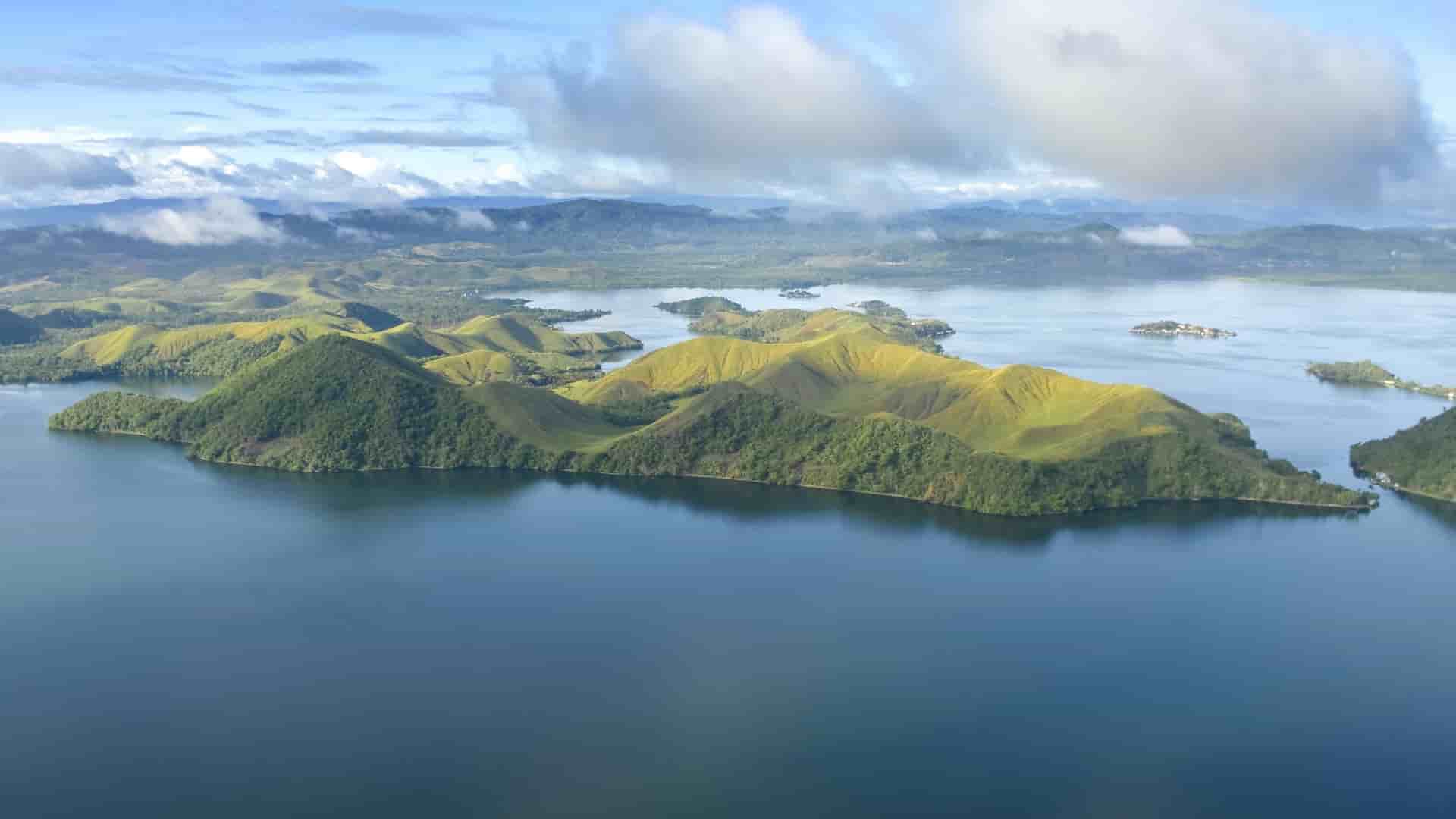 An aerial view of the verdant, rolling hills and a peninsula jutting out into the deep blue waters of Vanimo, a picturesque coastal town in Papua New Guinea.