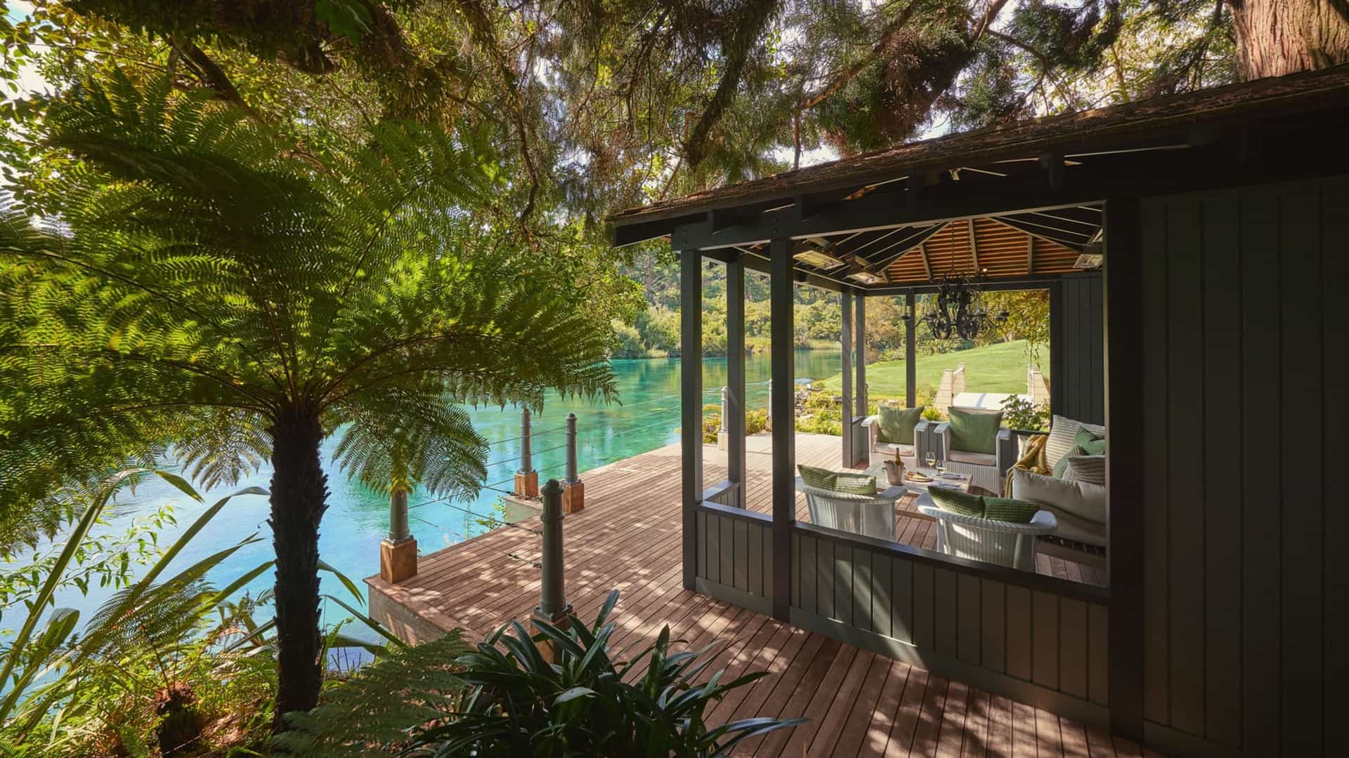 A covered outdoor lounge at Huka Lodge, New Zealand, overlooking a turquoise river surrounded by native fern trees.
