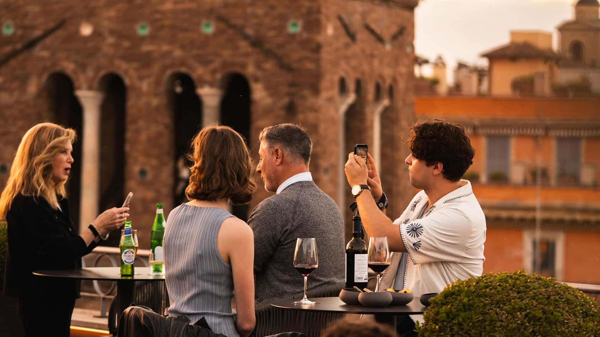 Guests enjoying wine on a rooftop terrace with the Iconic Pantheon Hotel in the background at dusk in Rome, Italy.