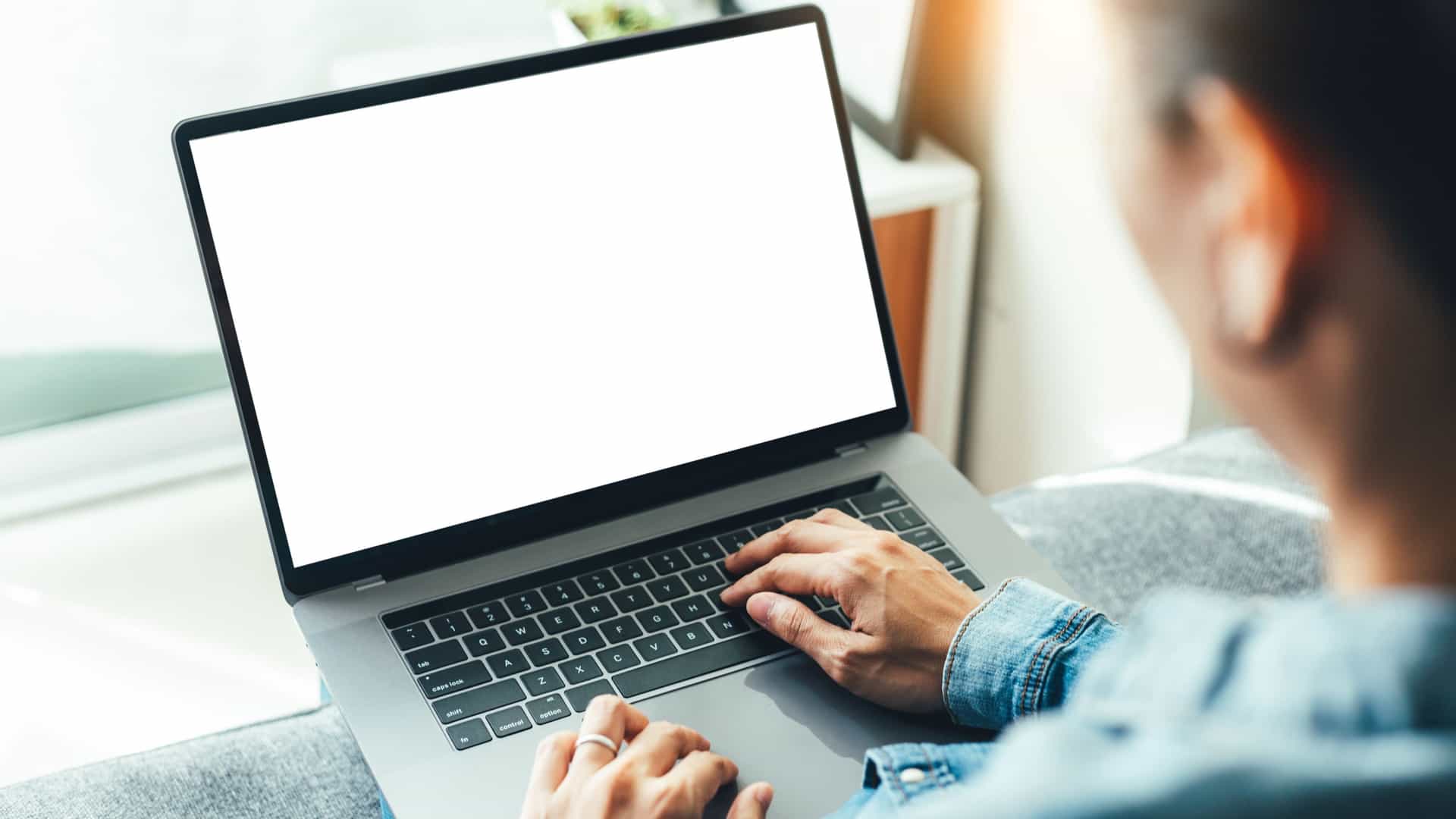 A person typing on a modern laptop with a blank white mockup screen.