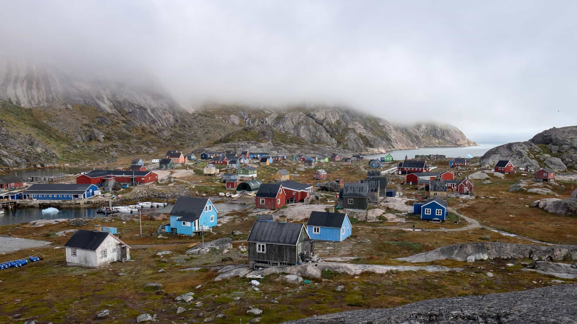 A traditional Greenlandic coastal village with vibrant, colorful houses built on rocky terrain beneath fog-covered Arctic mountains during a Silversea expedition cruise..
