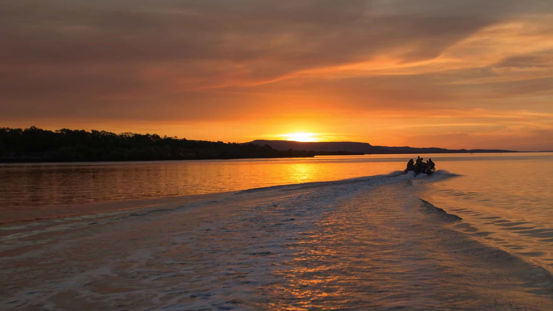 Silversea expedition cruise guests riding a Zodiac boat at sunset along the rugged coastline of the Kimberley region in Australia.