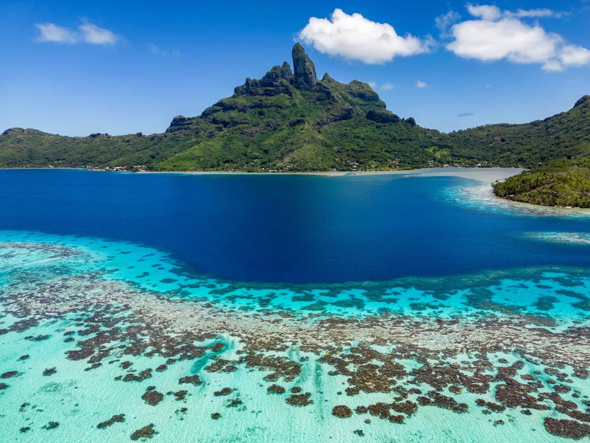 An aerial perspective of the coral reefs, turquoise lagoon, and Mount Otemanu in Bora Bora, French Polynesia, during a luxury cruise excursion.