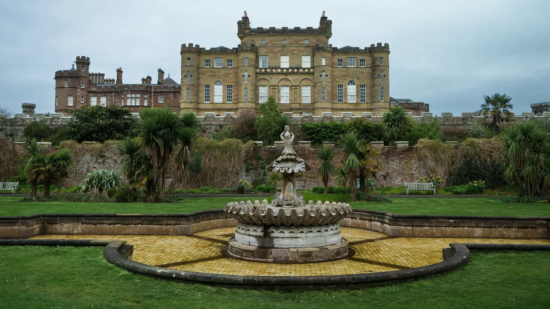 Culzean Castle in Scotland, featuring its majestic stone facade, tiered castle walls, and a classic stone fountain inside the formal fountain court gardens.