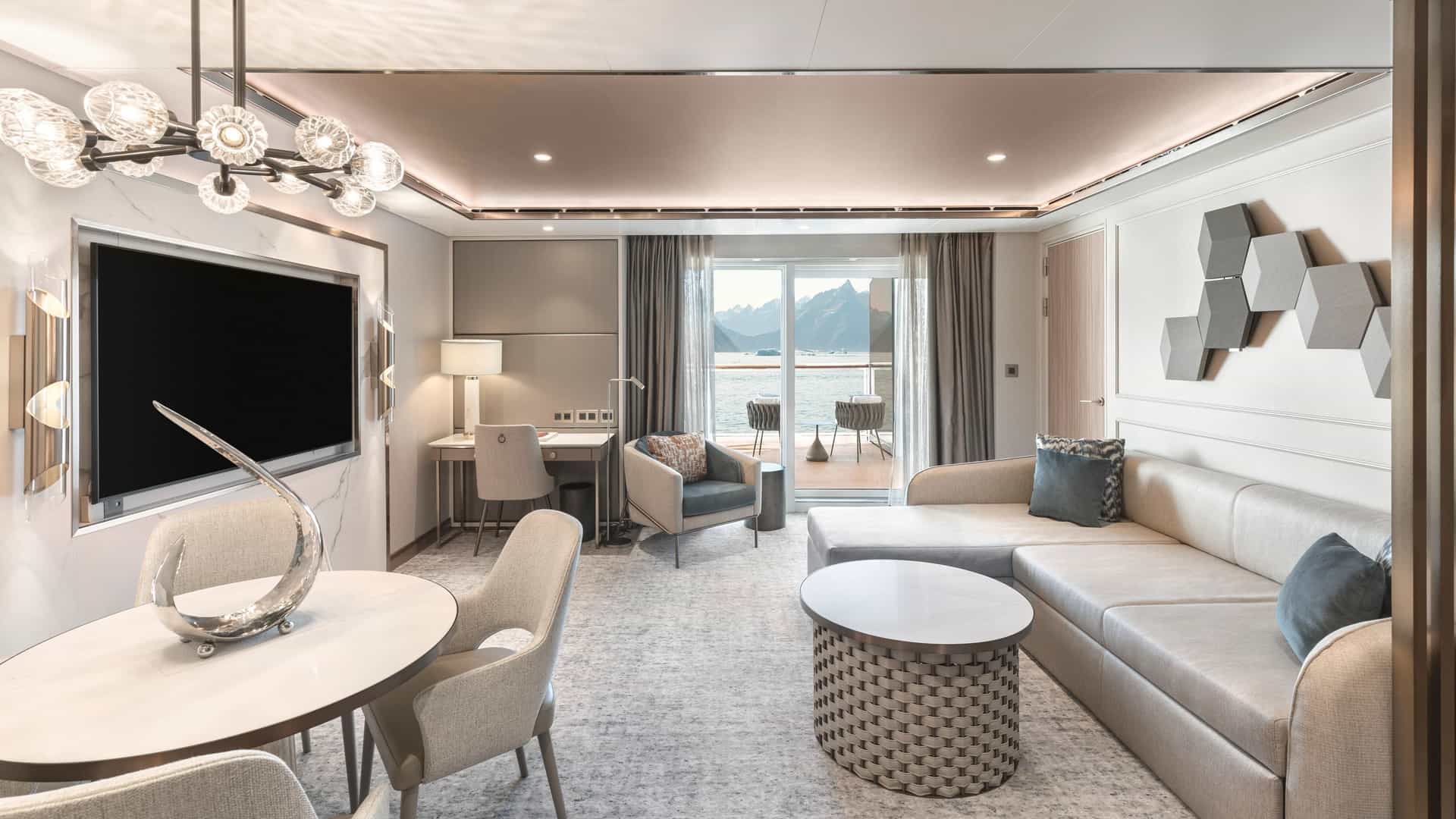 The elegant living room interior of a luxury Signature Suite onboard the Silver Endeavour expedition ship, featuring an open layout, plush seating, a dining area, and a private veranda overlooking polar mountains.