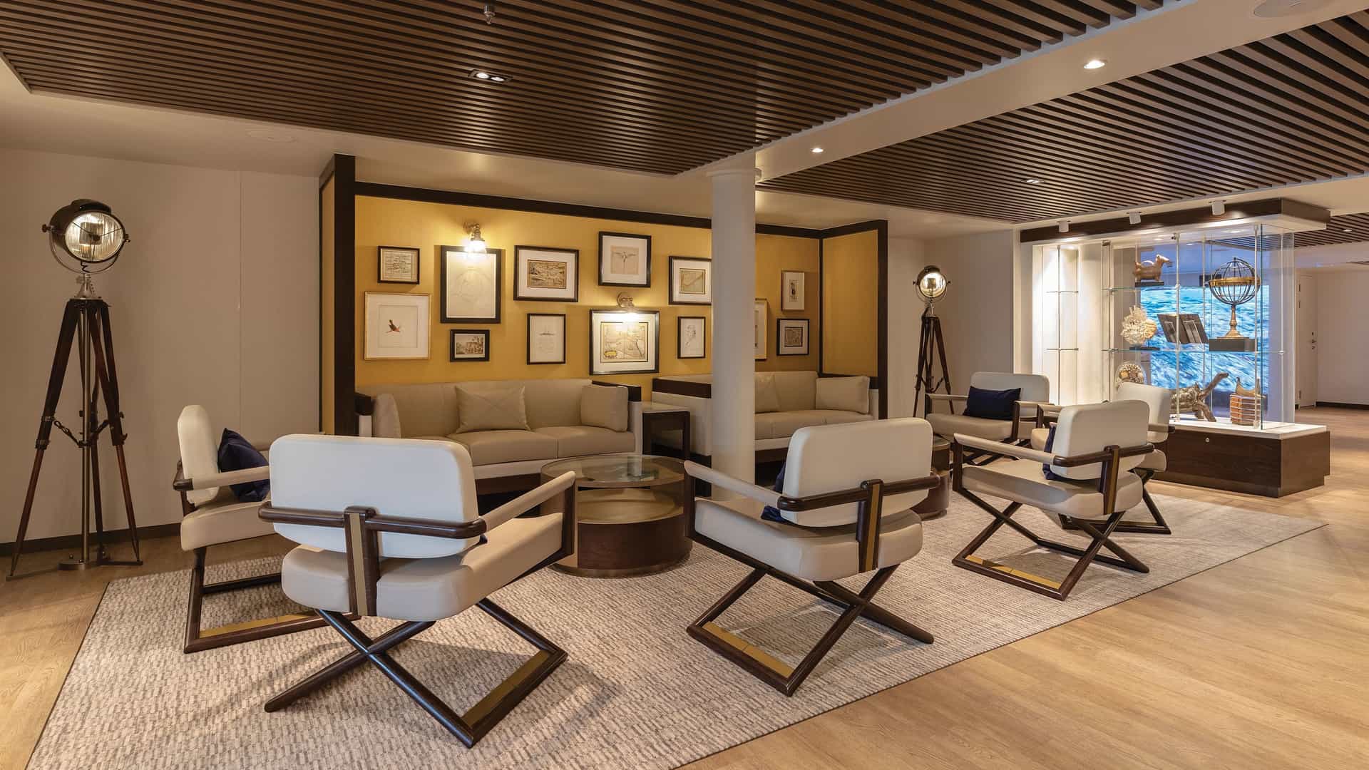 The sophisticated interior design of the Basecamp lounge on the Silver Origin expedition ship, featuring an intimate seating area and a gallery wall with historical maps and sketches.