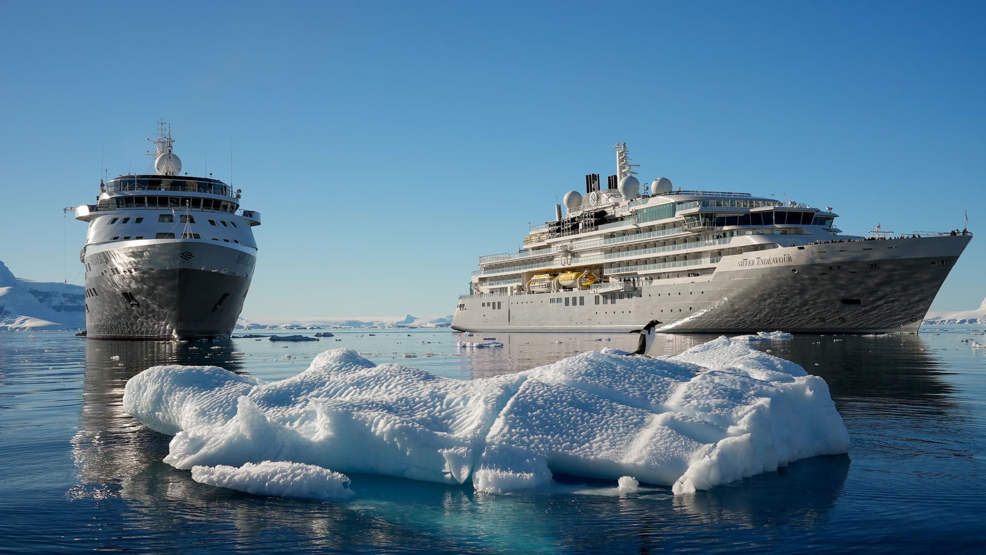 Two Silversea expedition ships, Silver Wind and Silver Endeavour, anchored in calm Antarctic waters surrounded by floating ice and snow-covered mountains.