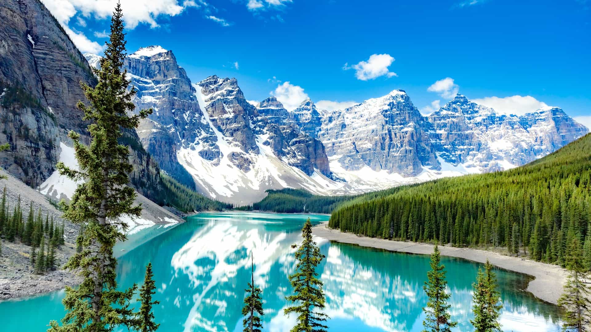 Scenic view of snow-capped mountains and a turquoise glacial lake surrounded by evergreen trees in Alaska on a Tauck cruise tour.