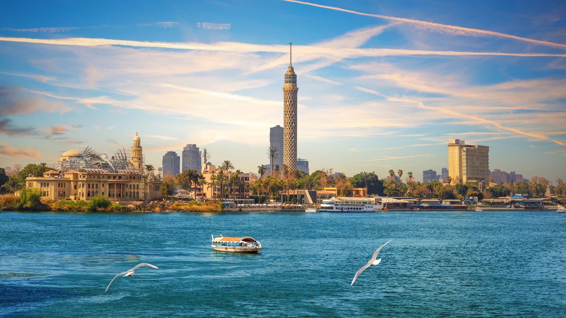 Scenic view of the Cairo Tower rising above the Nile River with a small boat and flying seagulls on a Tauck Egypt tour.