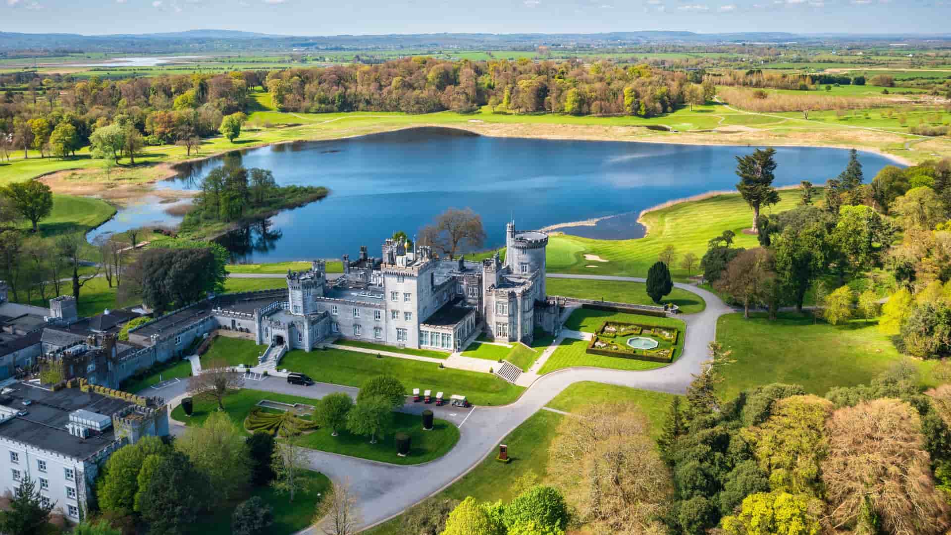 An aerial view of Dromoland Castle in County Clare, Ireland, surrounded by lush green lawns, a lakeside golf course, and rolling countryside, highlighting the grandeur of this historic estate often visited on Ireland cruise excursions.