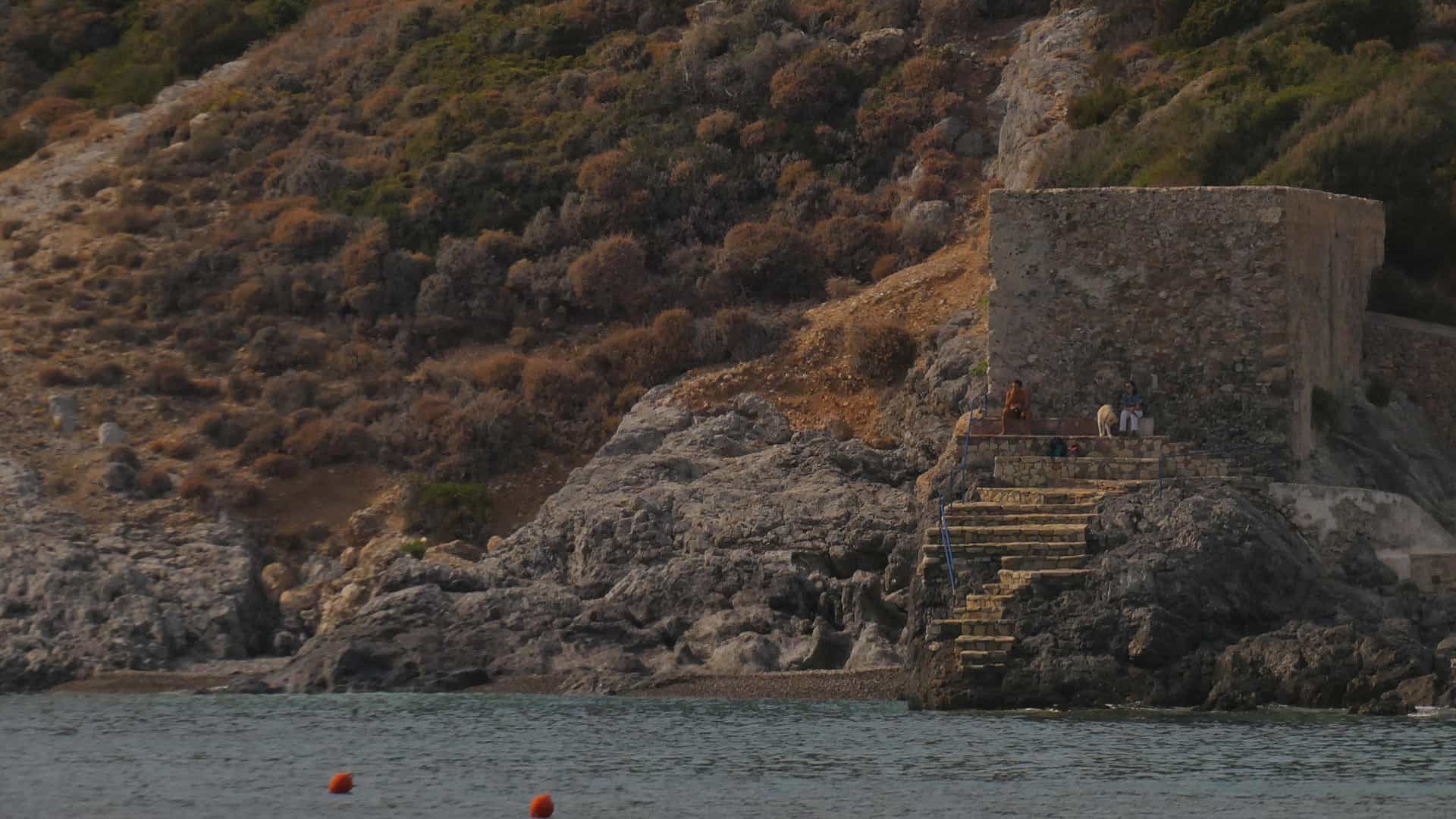 Kapsali's twin crescent bays at golden hour, with the Venetian castle of Chora crowning the hill above and the rocky islet of Chytra on the horizon
