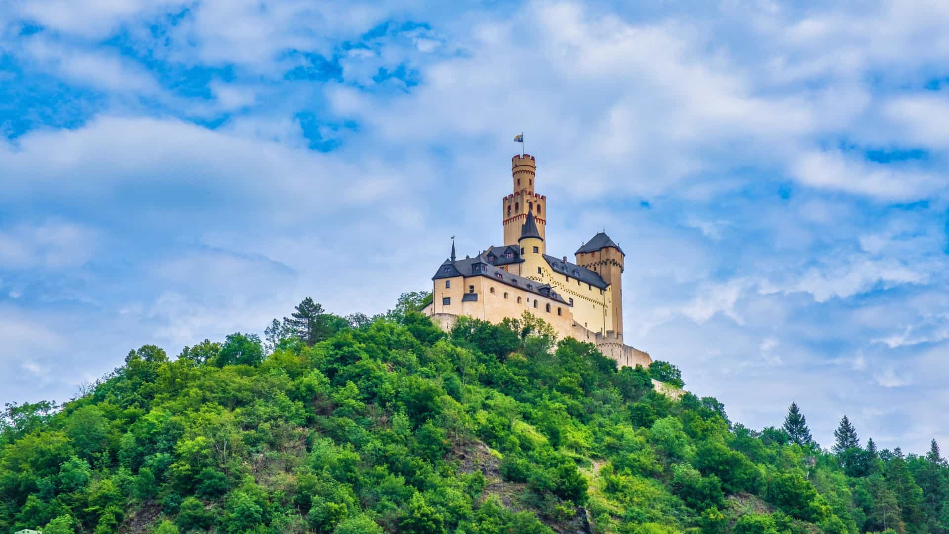 A magnificent medieval castle sits atop a lush green hill, with a dramatic cloudy sky in the background. This stunning sight is a highlight of a Uniworld river cruise through Northern Europe.
